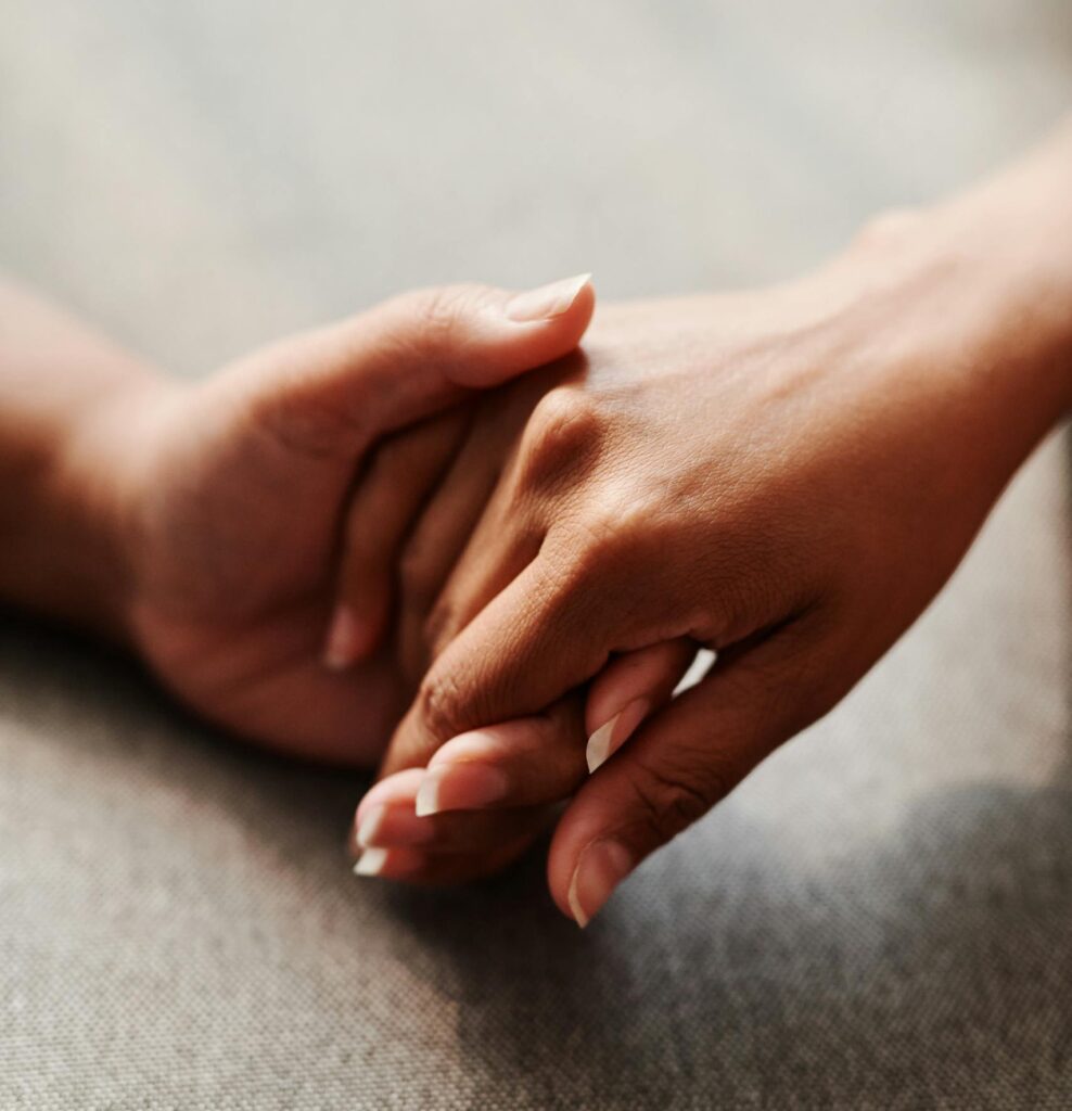 A close-up of two hands clasped together on a grey textile background, symbolizing unity.